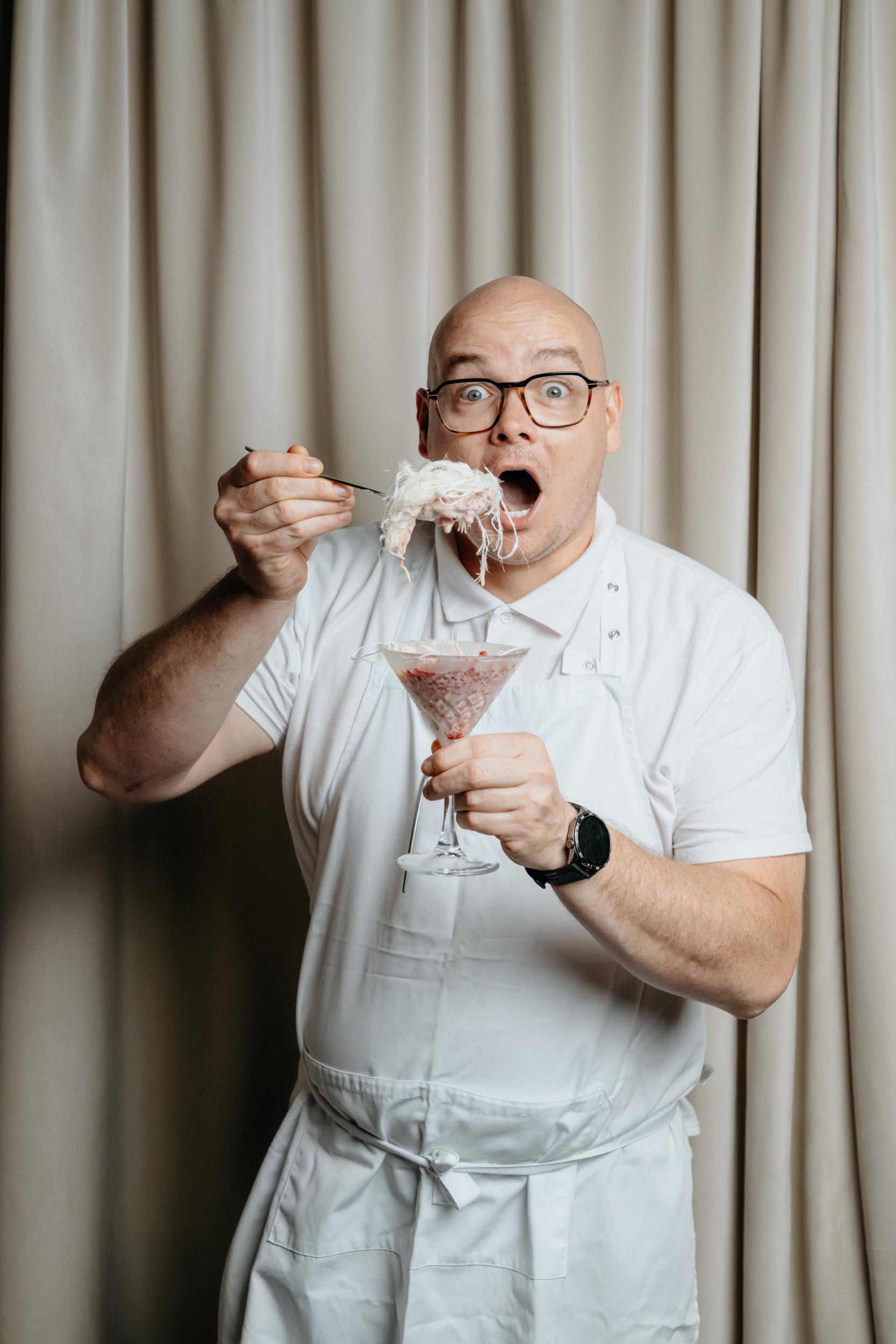 Michał Pezda, head chef at VODA, in a white jacket and apron, raising a spoonful of dessert