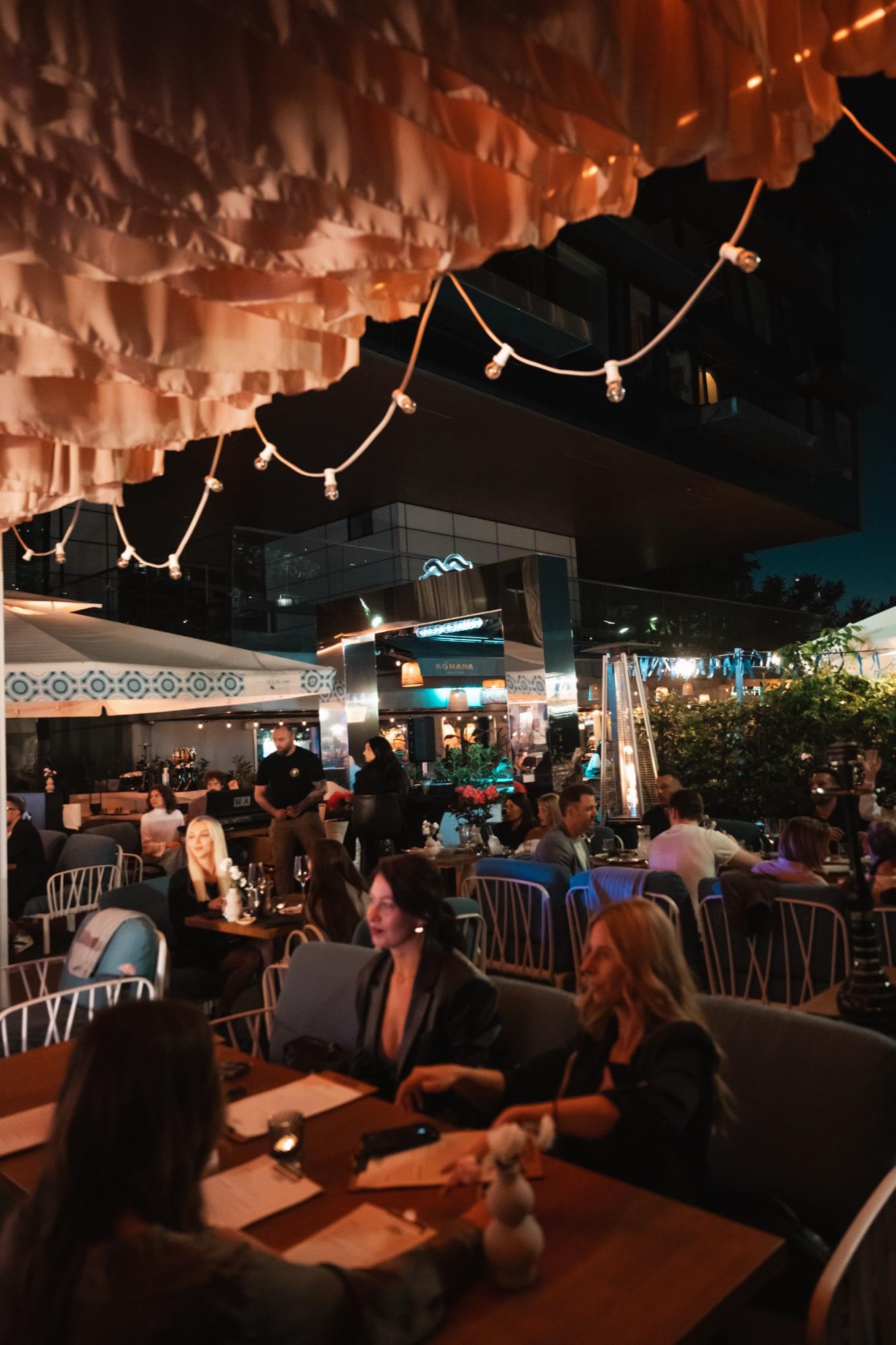 VODA's garden in the evening, full of guests at tables, with string lights under the wavy pergola ceiling.