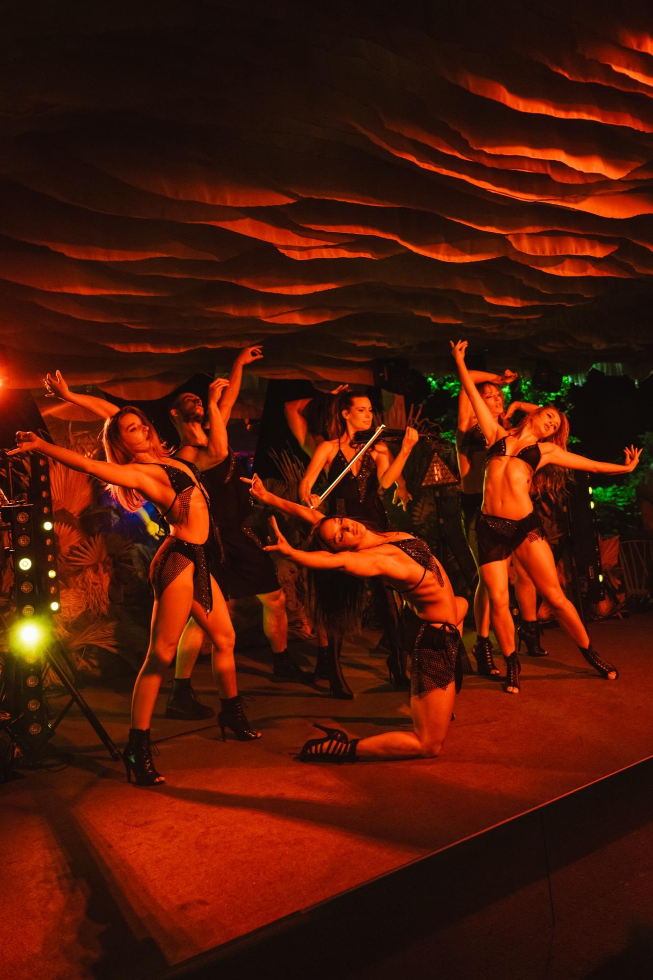 A group of dancers in motion on stage in red light.