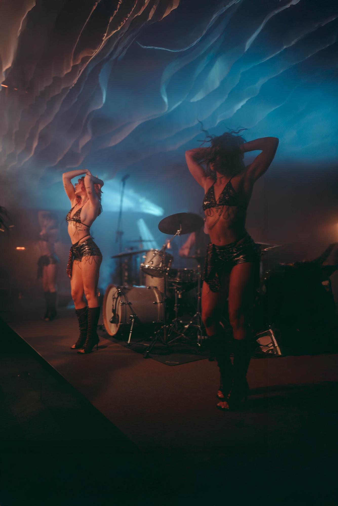 Two dancers on stage in blue light, with the band's drum kit behind them.