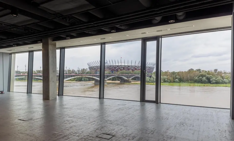 The Tides space on the second floor: an empty hall with a concrete ceiling and a glass wall, with the Vistula, the Poniatowski Bridge and the National Stadium beyond